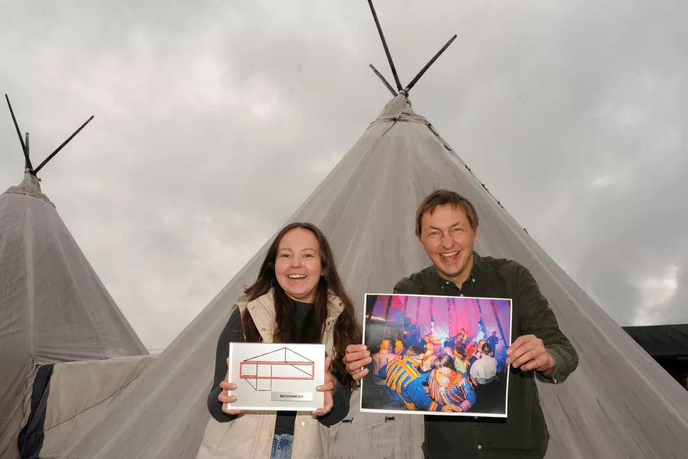 To personer står foran en lavvo og smiler stort. Personen til venstre holder frem en pris med logoen for Norske Kulturarrangører og personen til høyre holder frem et fargerikt fotografi. Foto. 