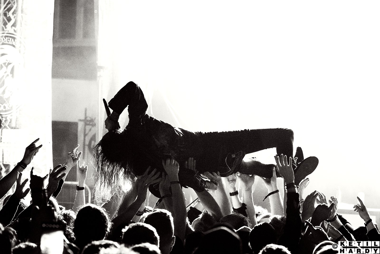 Artist med mikrofon crowdsurfer på rygg over publikum. Publikum strekker hendene i været. Foto. 