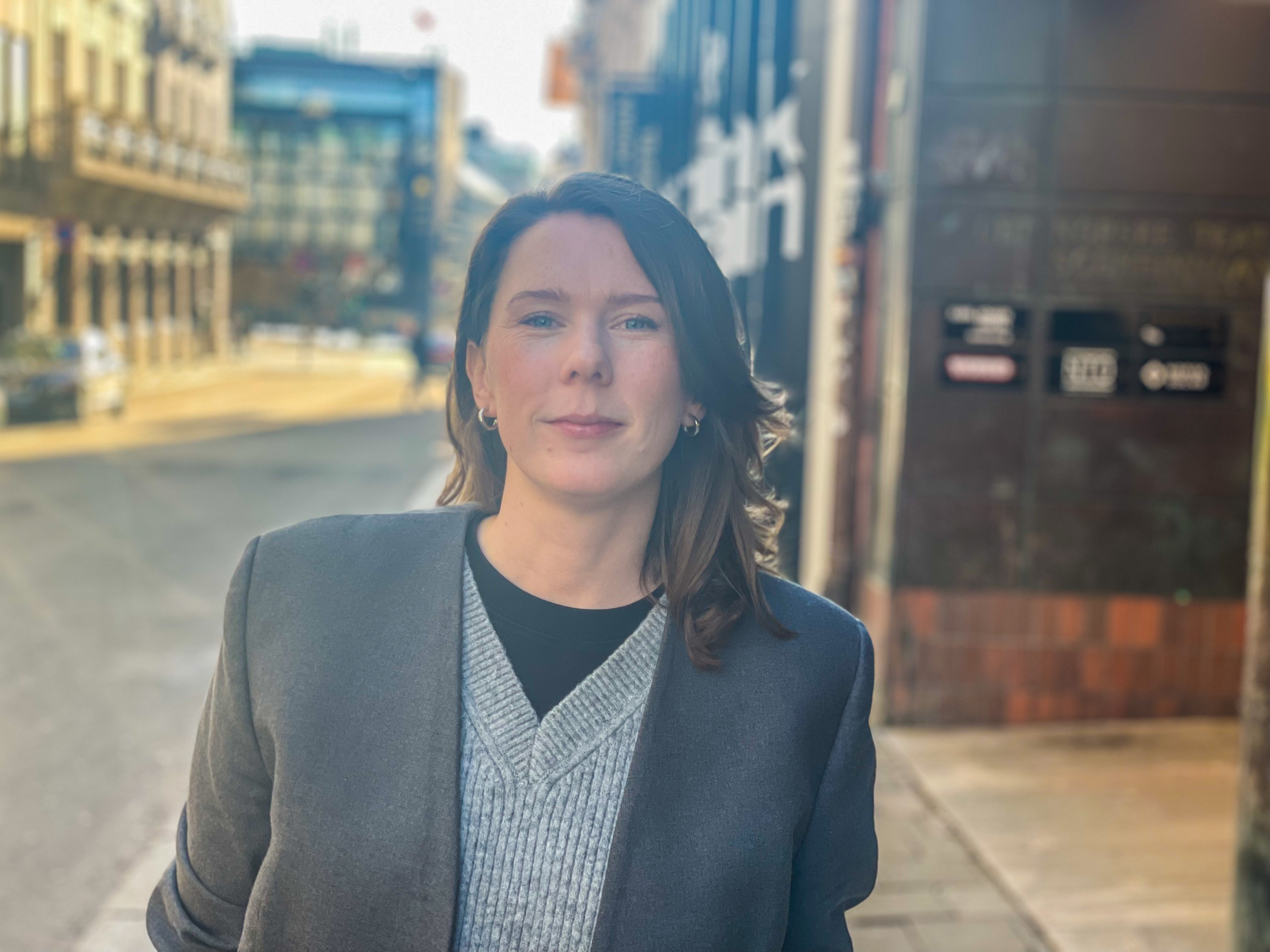 Jenny står utenfor NKAs lokaler og ser rett i kamera med et lite smil om munnen. 