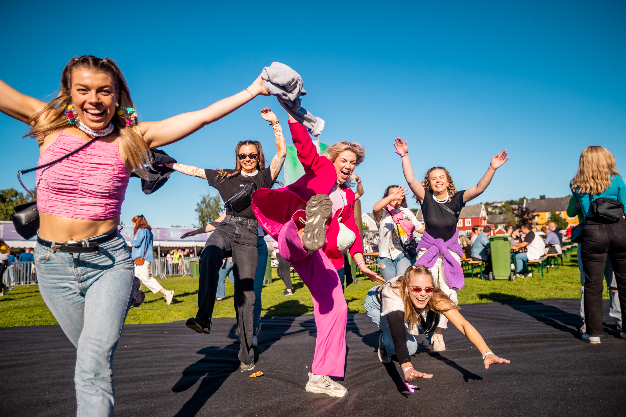 En sprudlende gruppe ungdommer løper og hopper av glede på et utendørs festivalområde. 