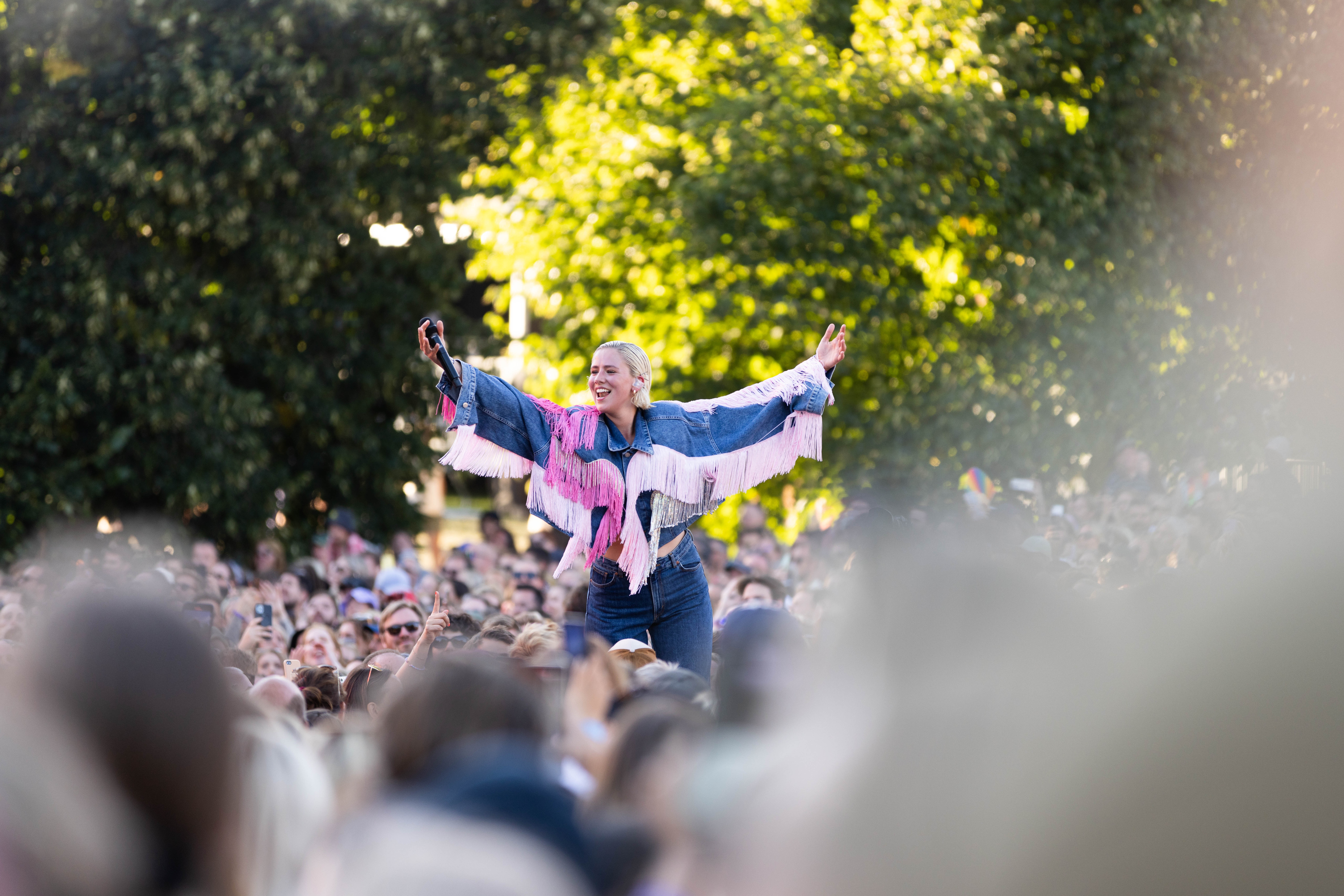 En fornøyd Dagny står på en forhøyning midt i publikum i Tøyenparken og strekker ut armene for å invitere til allsang. 