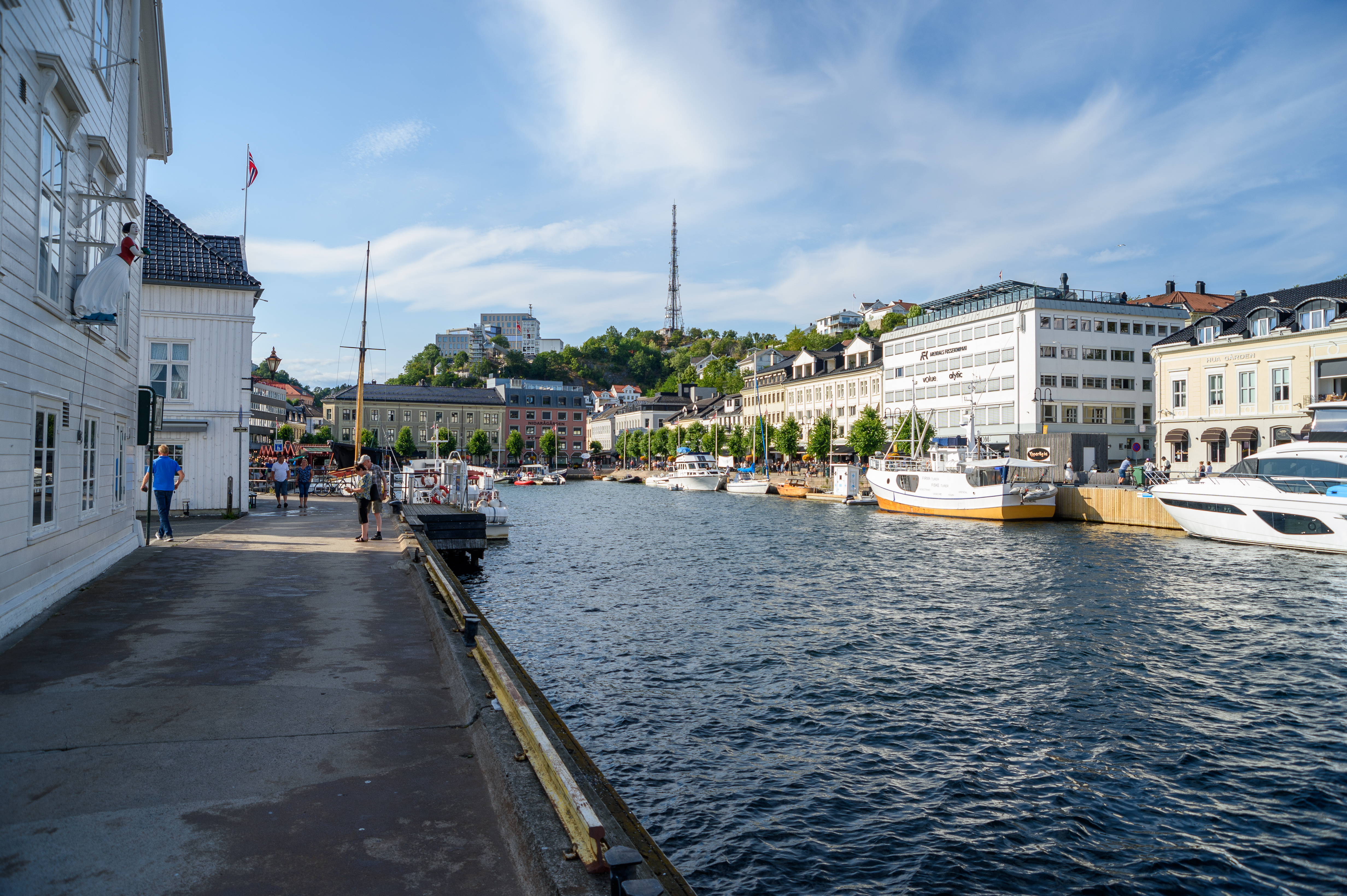 Sommerdag ved pollen i Arendal. Blå himmel og lette skyer, båter ligger til kai og langs pollen som er omkranset av eldre bebyggelse – både idylliske trehus og elegante murbygg. 