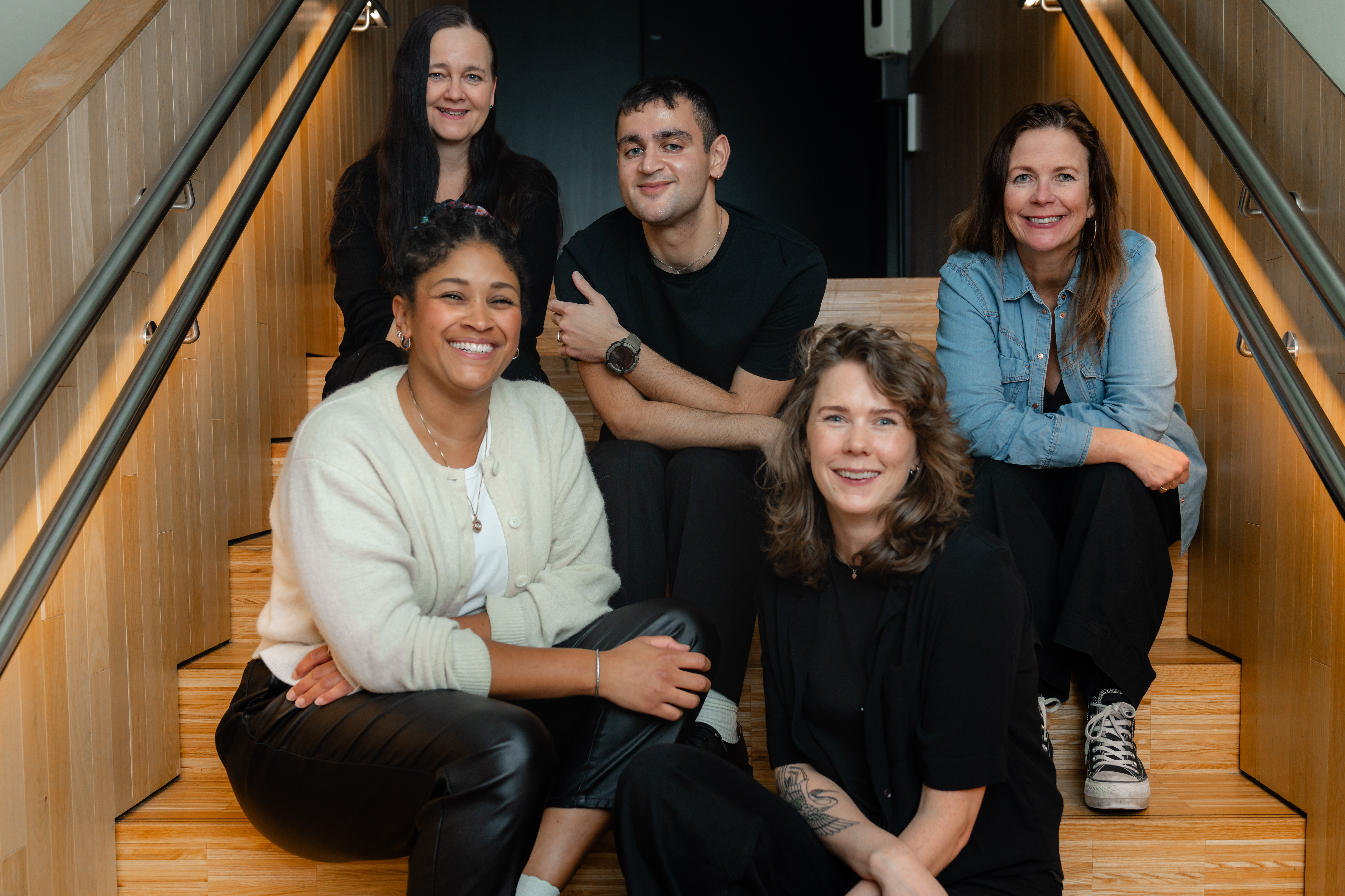 Administrasjonen i NKA sitter i en opplyst trapp og smiler fornøyd til kamera. 