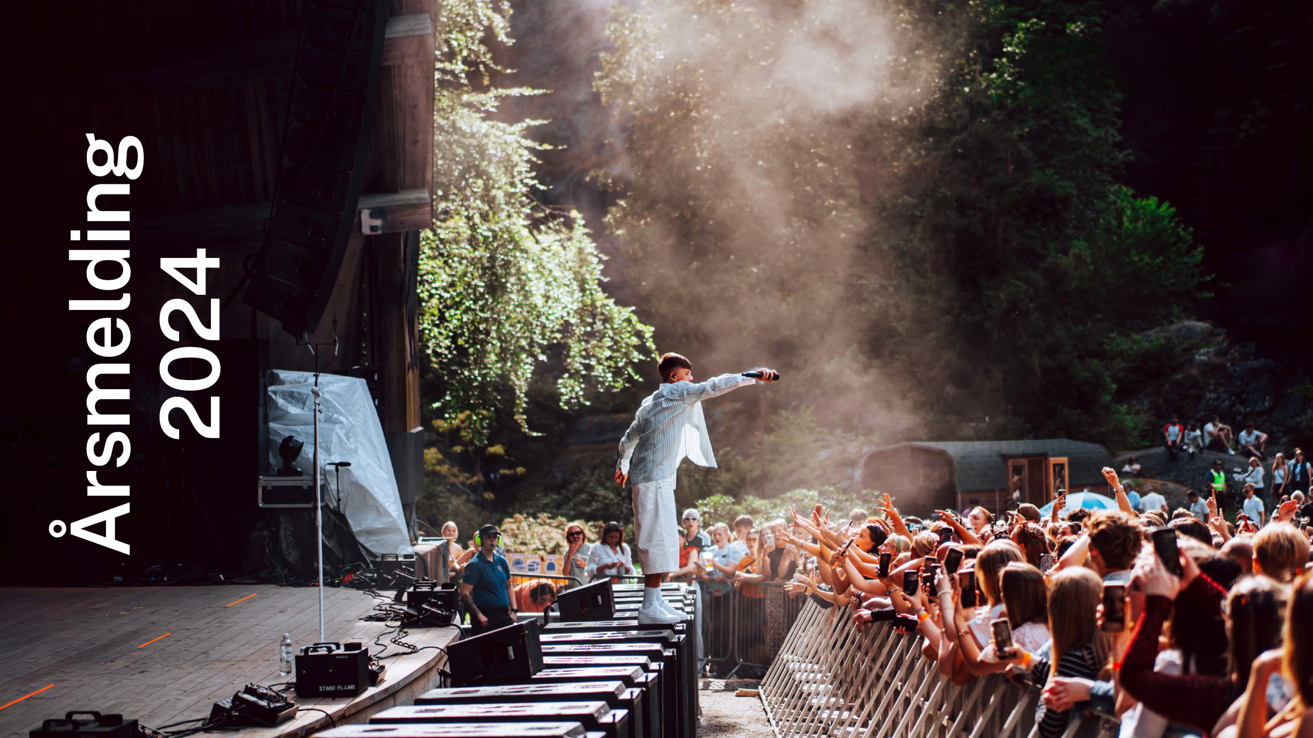 I grønne festivalomgivelser står en ung artist helt utpå scenenkanten og strekker mikrofonen mot et ivrig publikum. 