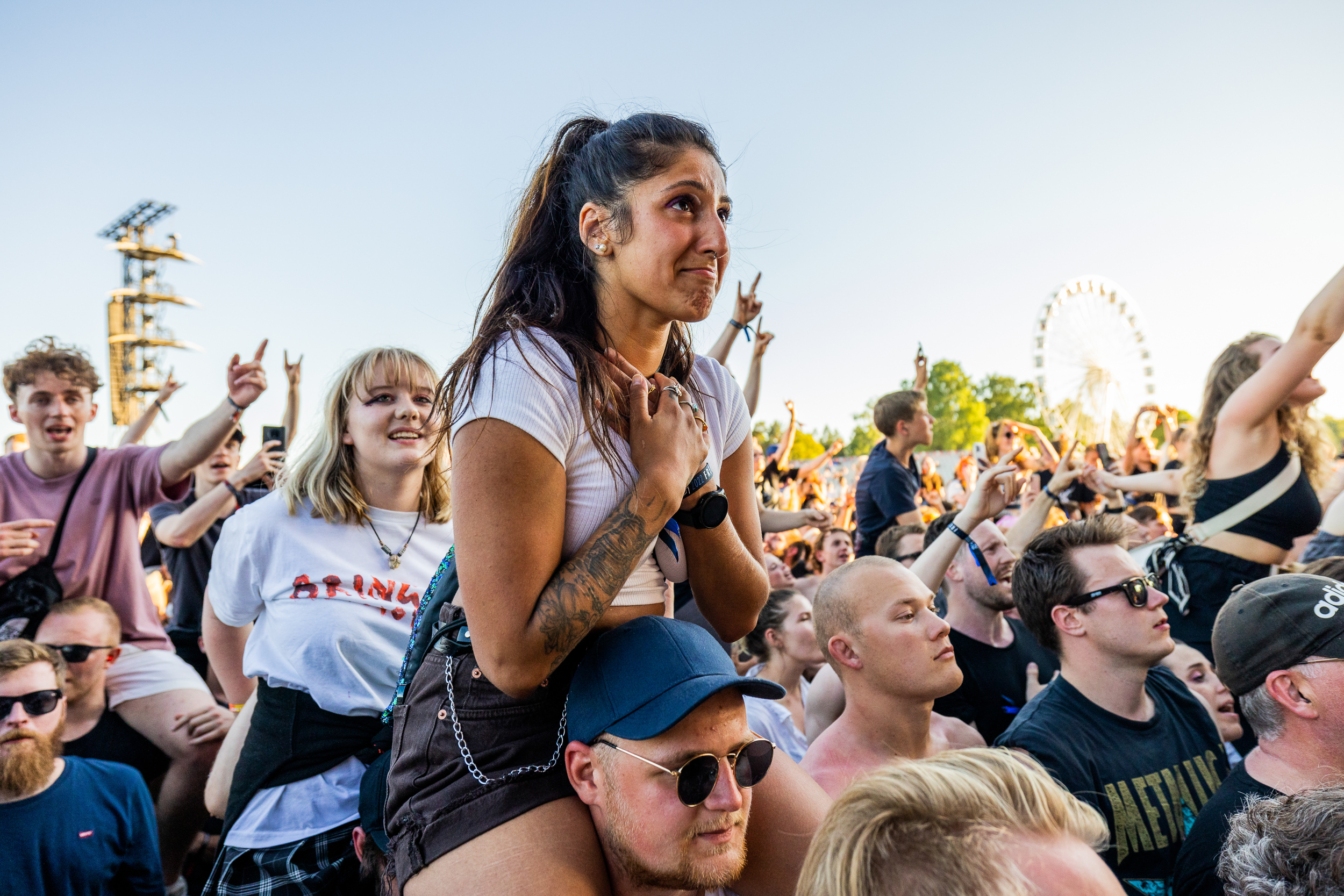 En kvinne sitter på skuldrene til en mann i en folkemengde som ser mot en konsert.