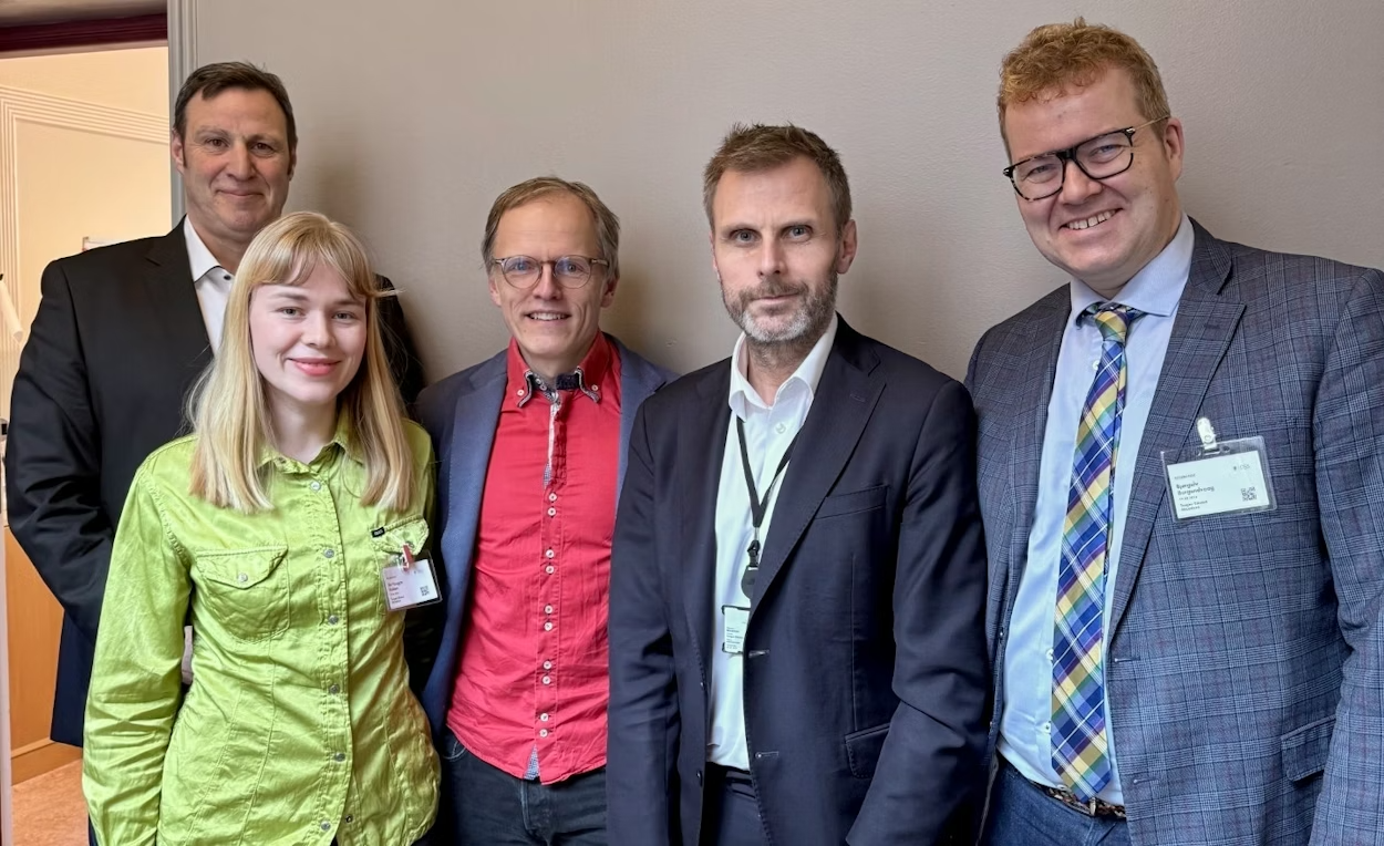 Fire menn og en kvinne står sammen og smiler til kamera.