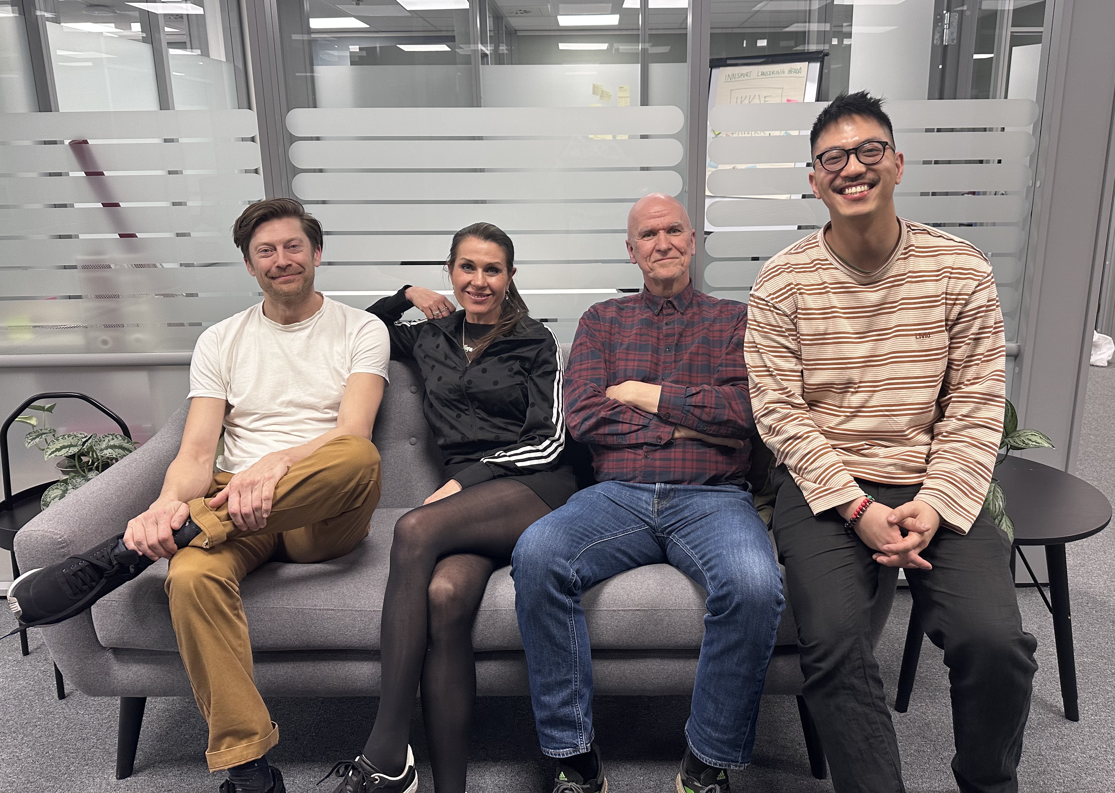 Fire smilende mennesker i en sofa ser mot kamera.