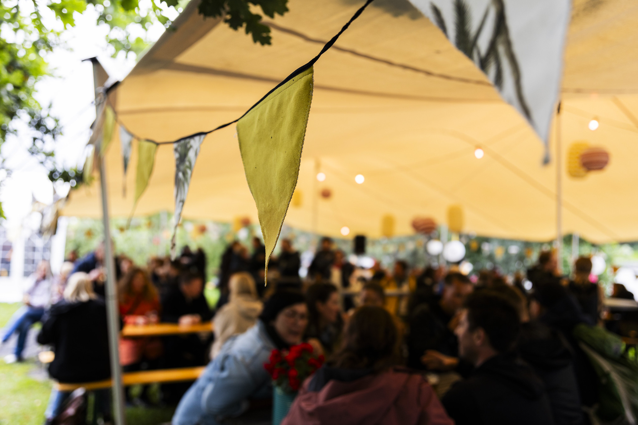 Nærbilde av vimpler som henger foran et telt med masse mennesker på et festivalområde.